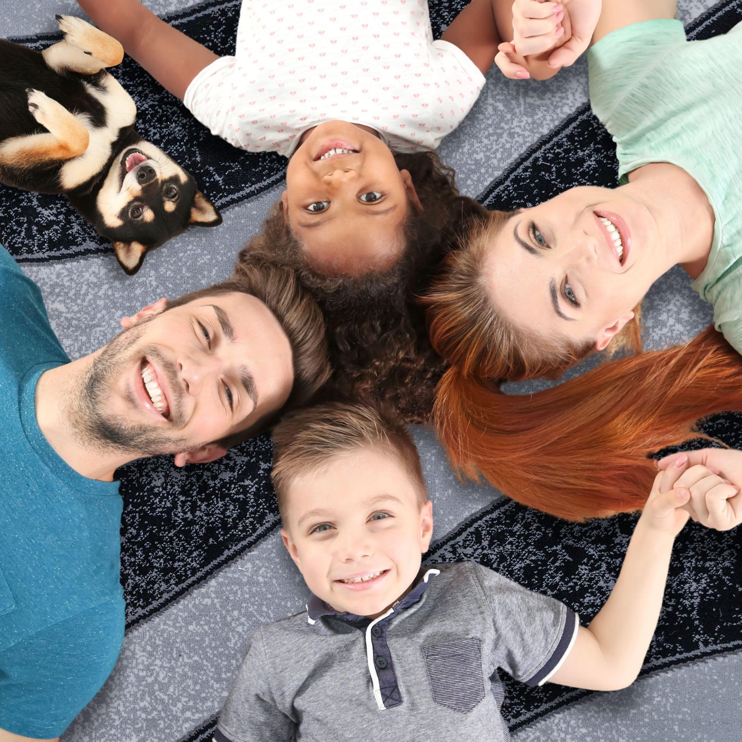 A family of four lying on the Black Wave Turkish rug with their dog, showcasing the rug’s soft surface and spacious comfort for quality time together at home