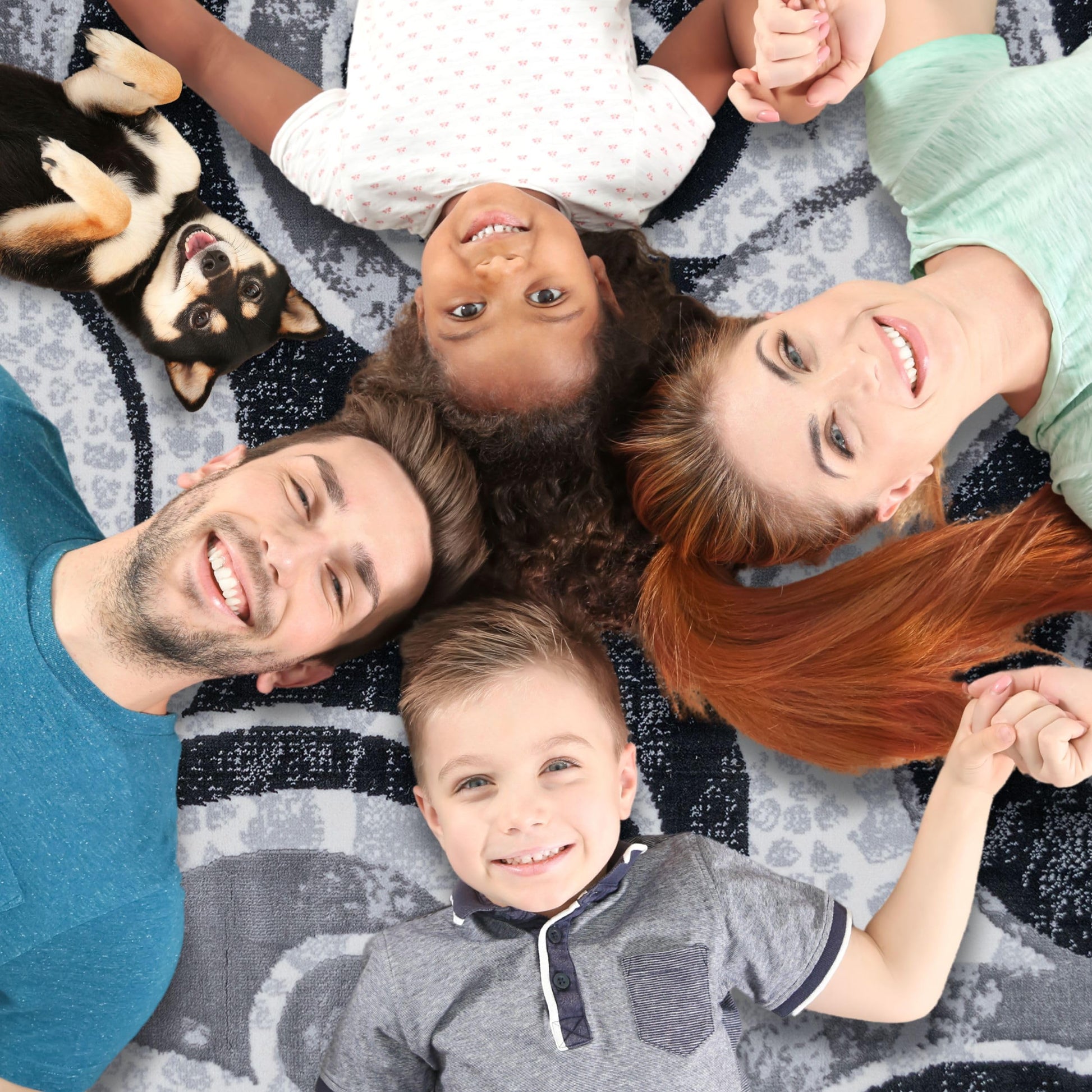 A family of four lying on the Black Swirl Turkish rug with their dog, showcasing the rug’s soft surface and spacious comfort for quality time together at home